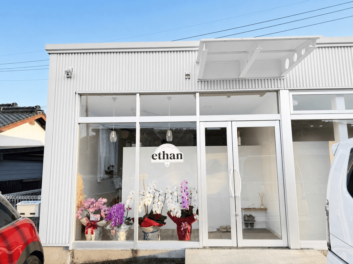 nail salon ethanのスタッフ。白いユニフォームでサロン内に佇む女性ネイリスト